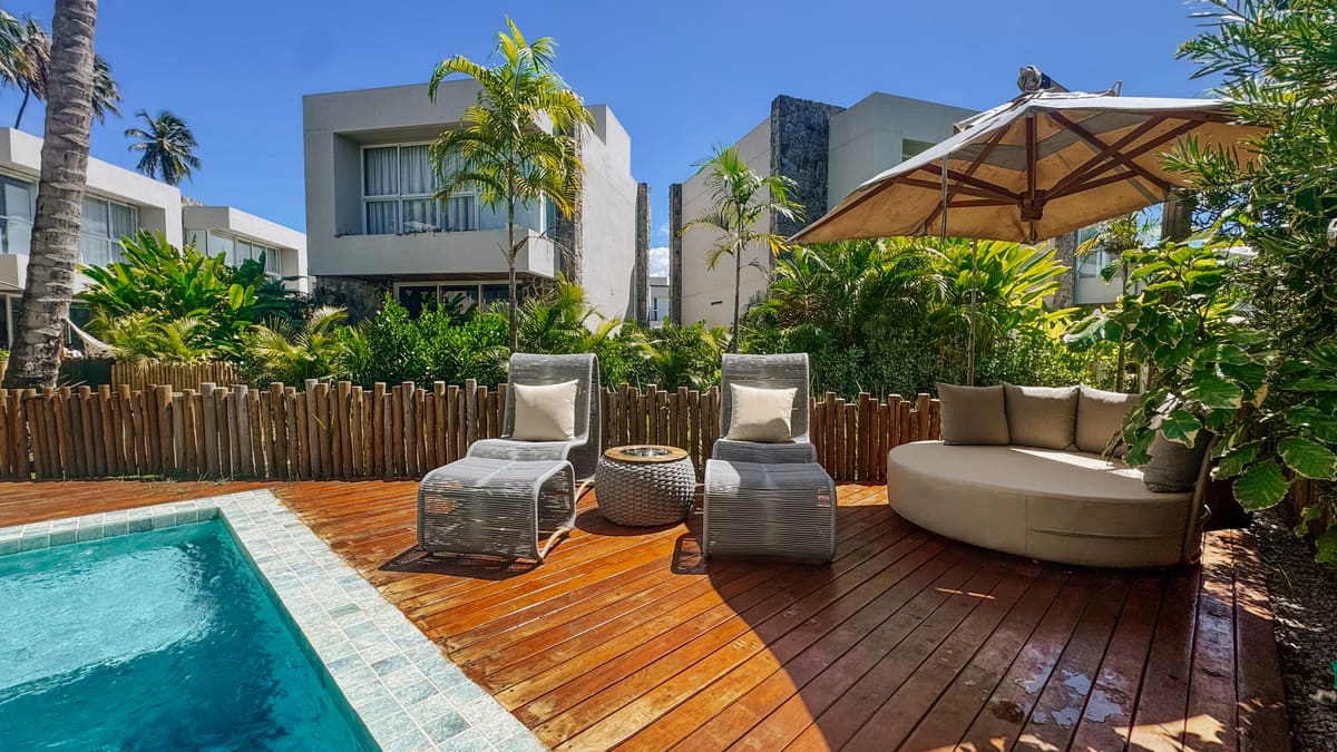 Deck de madeira com duas espreguiçadeiras, mesa lateral e chaise redonda sob ombrelone, borda da piscina à esquerda